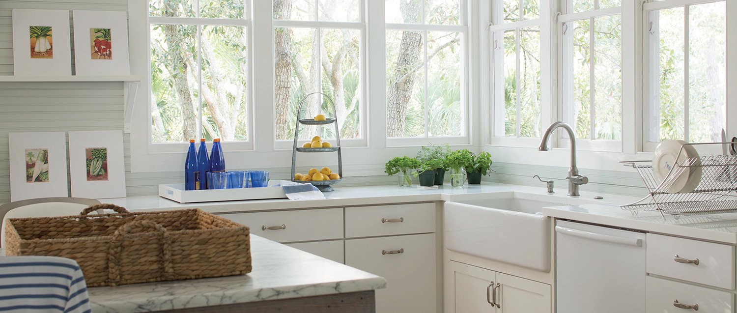 Kitchen with big windows, white cabinetry and an island with wicker tray on top